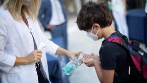 Un niño se desinfecta las manos después de que le tomen la temperatura a la entrada del colegio 