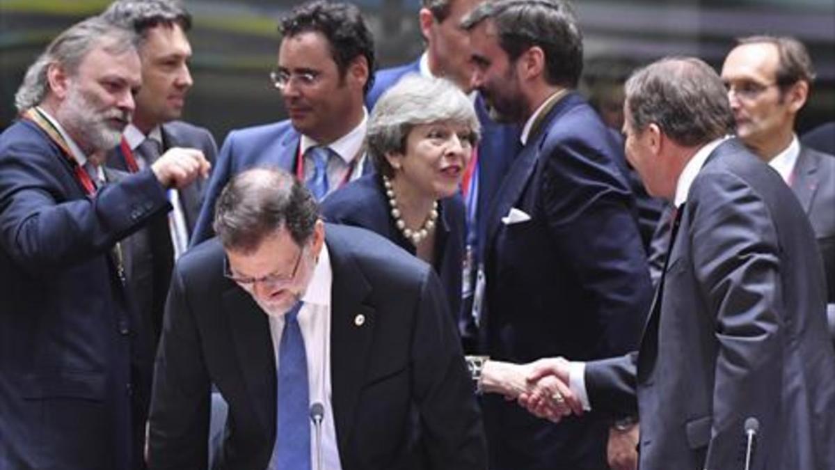 Rajoy, delante de May, toma asiento, durante la cumbre de ayer en Bruselas.