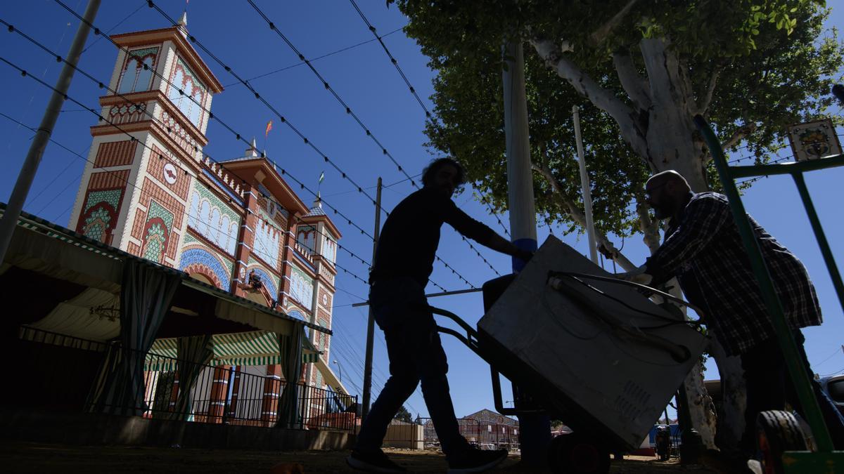 Dos hombres transportan una nevera para una de las casetas del recinto de la Feria de Abril de Sevilla