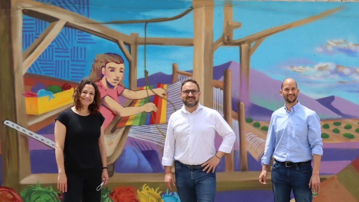 Isabel Casalduero, Diego José Mateos y José Ángel Ponce ante un mural en el que se homenajea la principal actividad artesanal de la pedanía de Coy.