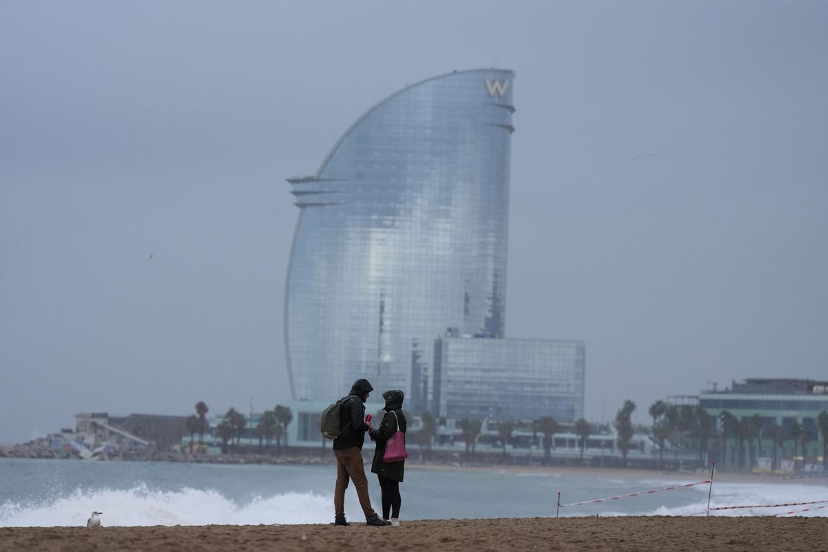Vecinos de Barcelona pasean bajo la lluvia en la playa de la Barceloneta durante el temporal, a 19 de enero de 2026, en Barcelona, Cataluña (España).