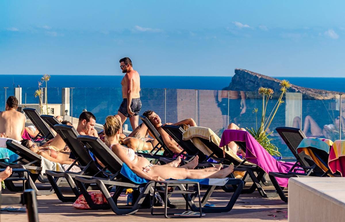 La azotea de un hotel de Benidorm, llena de turistas tomando el sol con la isla al fondo.