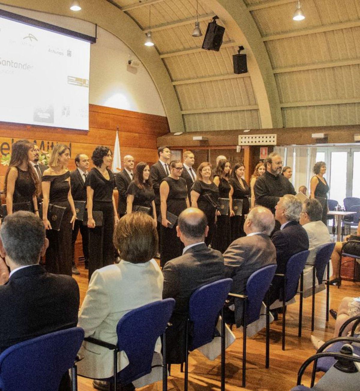 A la izquierda, el coro «El León de Oro» en La Granda; a la derecha, público en el salón de actos. | M. M. / C. G.