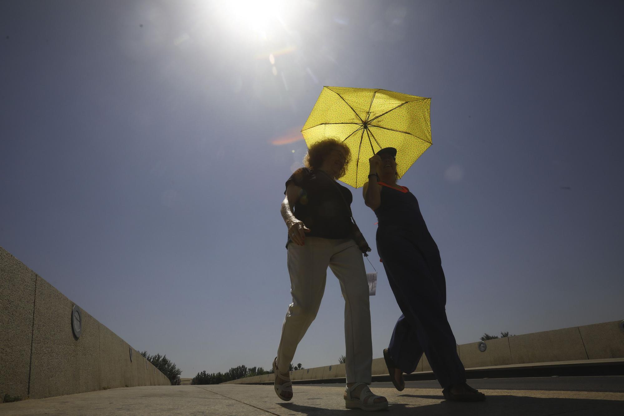 Dos personas camina en Córdoba refugiándose del calor.