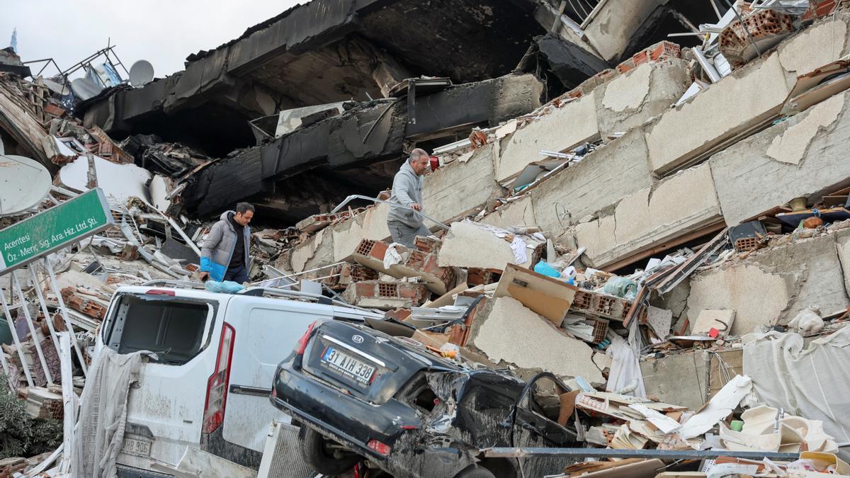 Cotxes xafats i persones buscant entre les runes d'un edifici