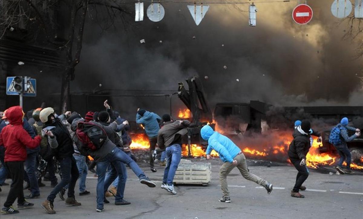 Varios manifestantes protegidos tras las barricadas lanzan piedras contra la policía ucraniana.