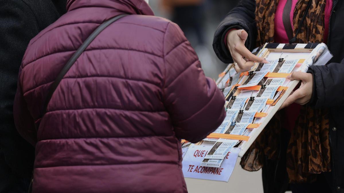 Una mujer compra un décimo de lotería a una vendedora ambulante días antes del Sorteo de La Lotería del Niño.