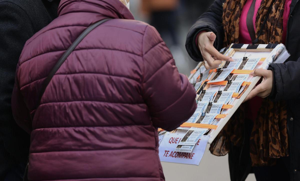 Una mujer compra un décimo de lotería a una vendedora ambulante.