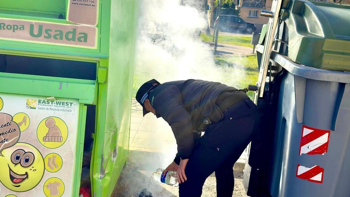 Un agente local echa agua en unas brasas encendidas junto a un contenedor.