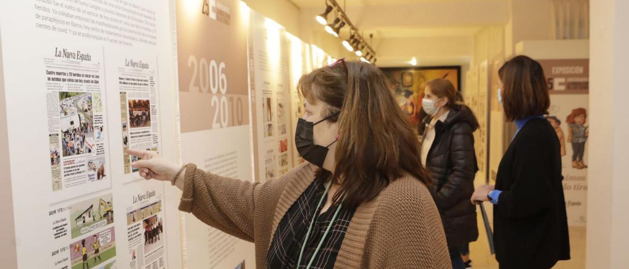 Sara Valiño, en primer término, señala una de las portadas de la exposición “Seguimos dando tira”, que conmemora los 25 años de LA NUEVA ESPAÑA de las Cuencas | Fernando Rodríguez