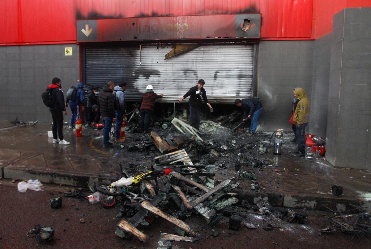 Trabajadores de supermercados inspeccionan los daños causados ​​por el fuego después de los enfrentamientos entre la policía y manifestantes antigubernamentales en Perú.