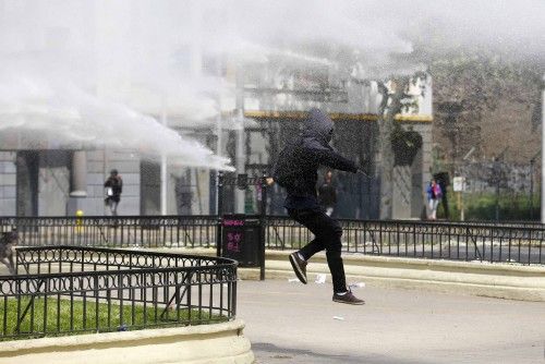A student protester runs from a jet of water released from a riot police vehicle during a demonstration to demand changes in the education system in Santiago