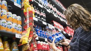 Una joven observa la etiqueta de un refresco en un supermercado