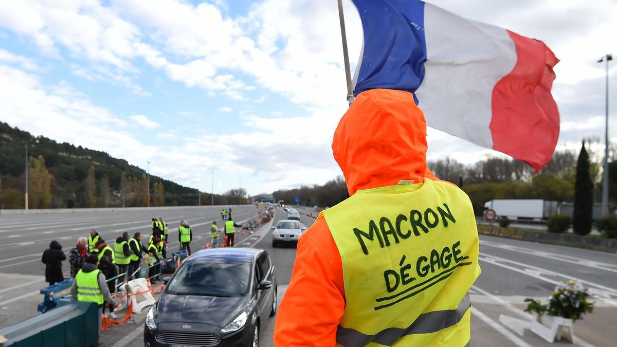 Un 'chaleco amarillo' con el lema 'Macron dimite' ondea una bandera francesa en una protesta en La Barque, cerca de Marsella, en diciembre de 2018.