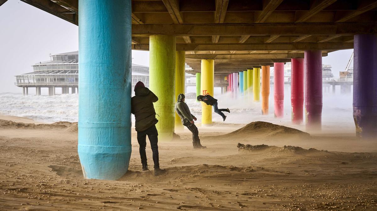 Gente jugando contra la fuertes rachas de viento de más de cien kilómetros por hora, en la playa de Scheveningen, Países Bajos