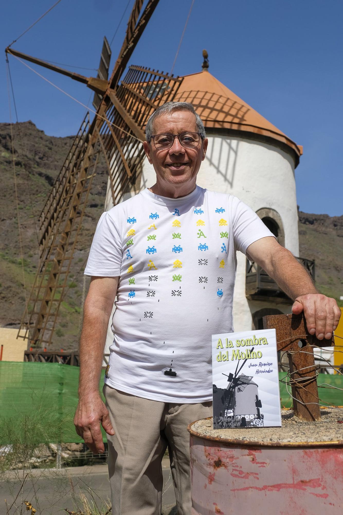 Juan Ramírez sostiene un ejemplar de su libro frente al Molino de Viento de Mogán.