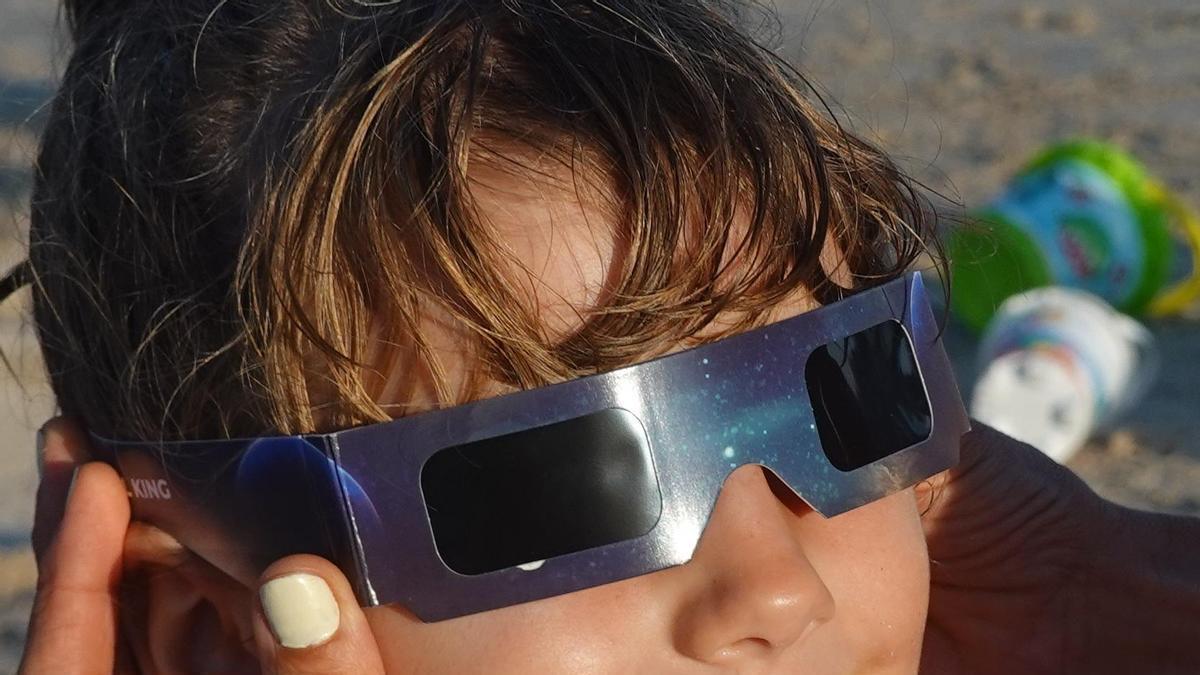 Un niño con gafas para el eclipse en una playa.