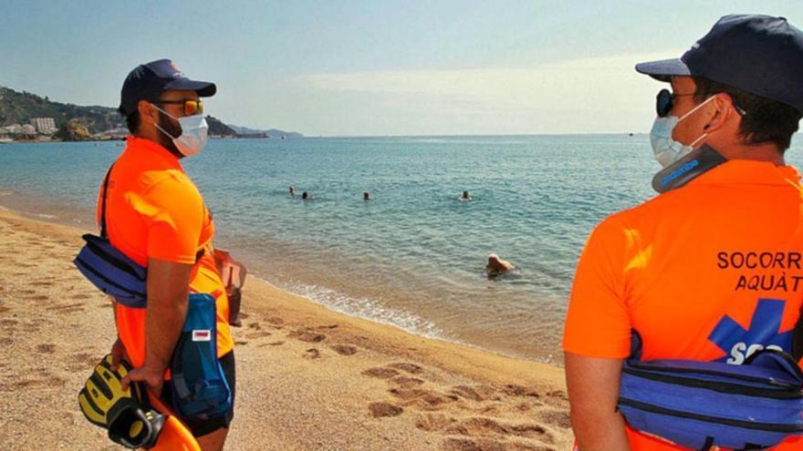 Dos socorristes amb mascareta vigilen una platja de Blanes mentre alguns banyistes estan a l&#039;aigua.