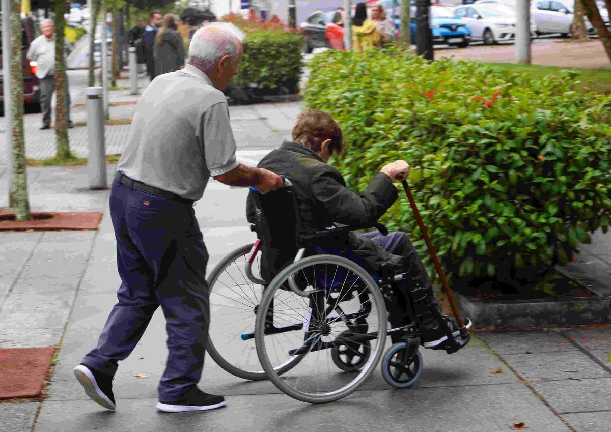 Un hombre empuja una silla de ruedas de una mujer con depedencia.