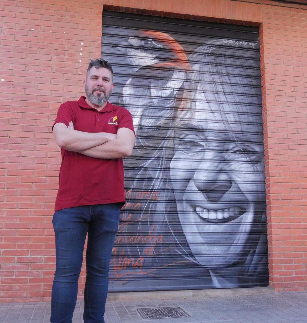 Saúl, propietario del negocio, con el grafiti de Robe a su espalda.