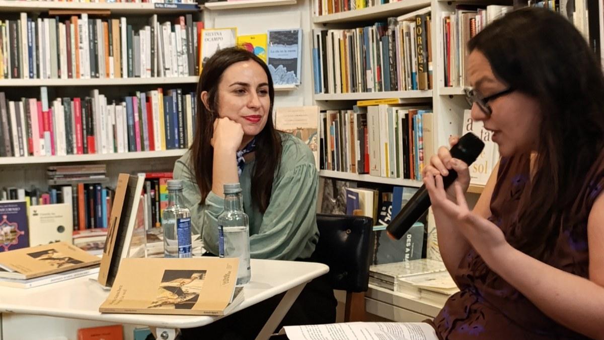 La poeta María Sánchez, a la izquierda, en Santiago, ante portadas de su libro ‘Fuego la sed’, escuchando la presentación de Faía Díaz en la librería Numax