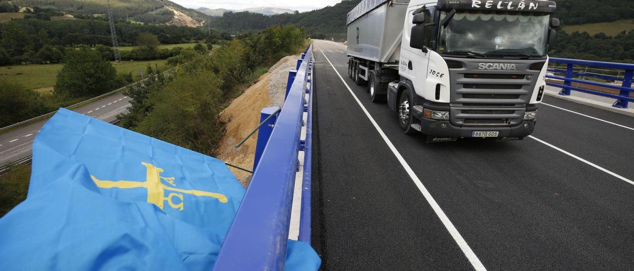 Un camión pasa sobre el puente de La Barrosa, abierto ayer, ante una bandera de Asturias colocada en la infraestructura. | Luisma Murias