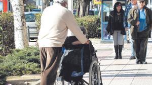 Un hombre pasea a una mujer en silla de ruedas.