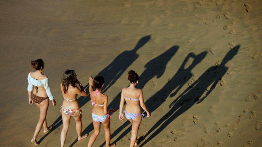 Un grupo de jóvenes pasean en bikini por una playa.