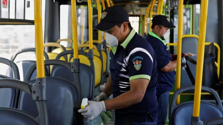 Trabajadores limpian protegidos con máscaras y guantes el interior de un autobús público en Guatemala.