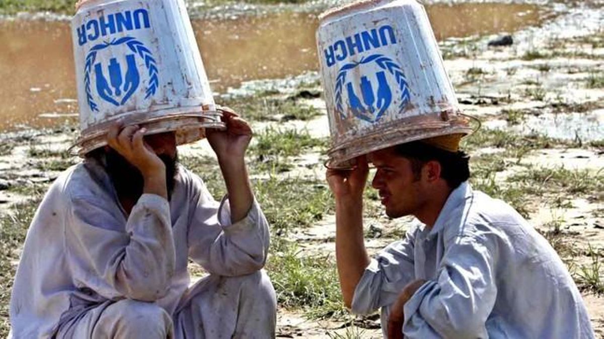 Dos afectats per les pluges es cobreixen el cap amb galledes buides de l’Alta Comissaria de l’ONU per als Refugiats.