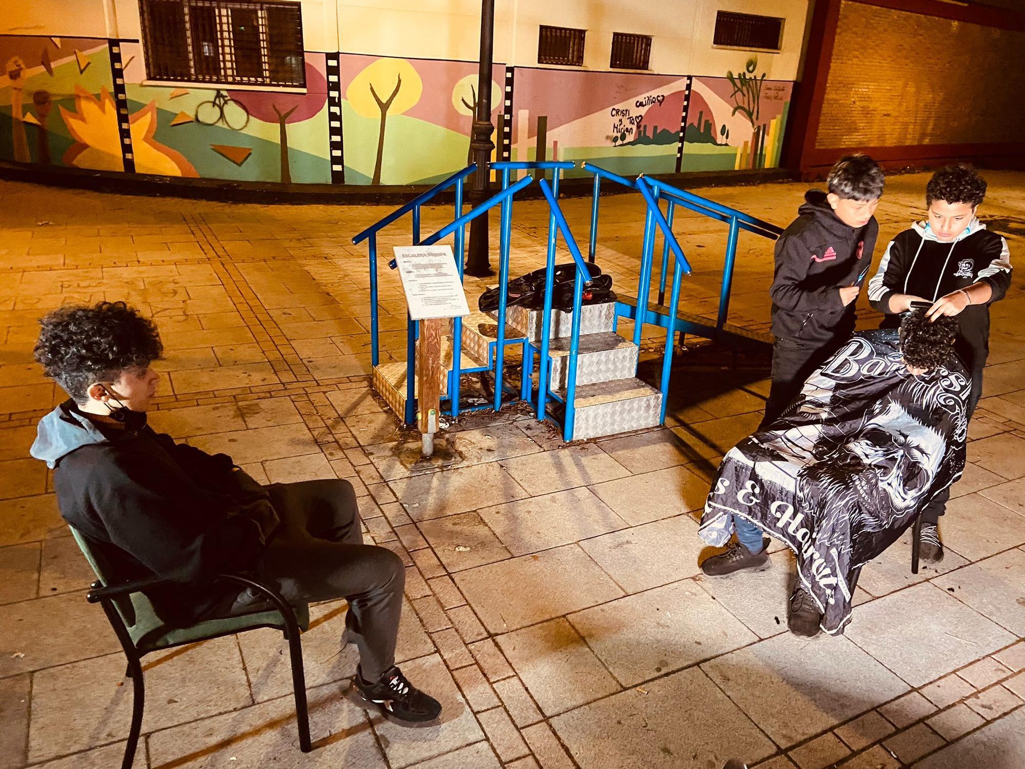 Alexis e Ilyas le cortan el pelo a Badr, mientras Reda observa en una plaza de San Cristóbal