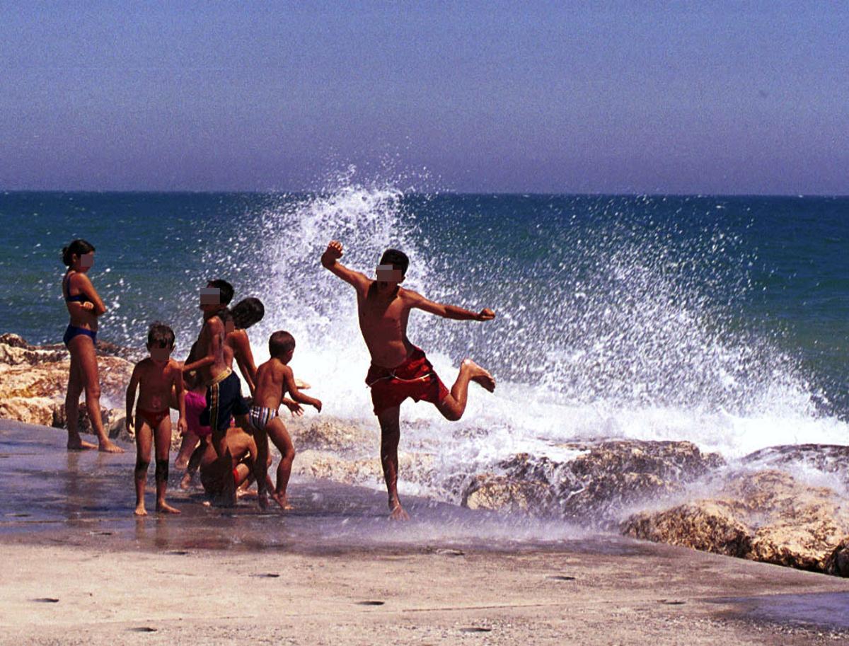 Niños juegan con las olas en un espigón de El Palo, en foto de archivo.