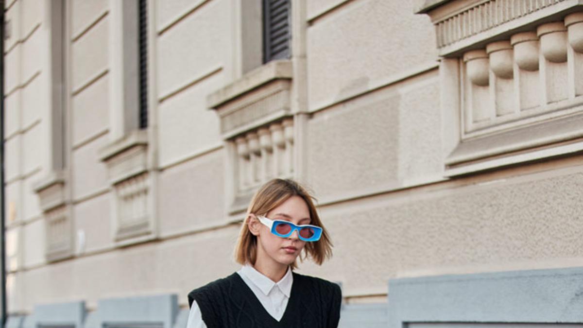 Look con camisa blanca, chaleco, bermudas de cuero y botas altas visto en el 'street style' de Milán