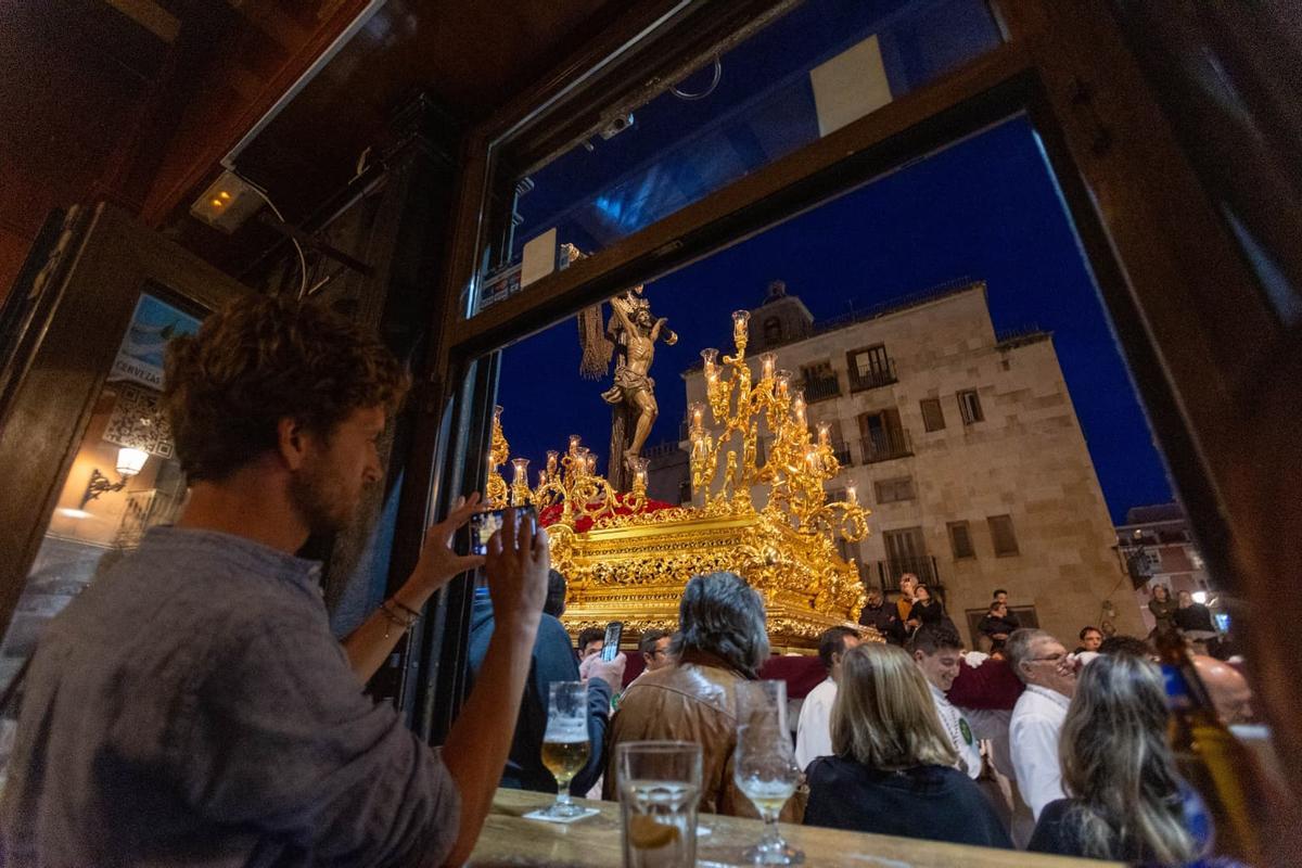 Un turista disfruta de unas vistas privilegiadas de una procesión desde la barra de un bar.