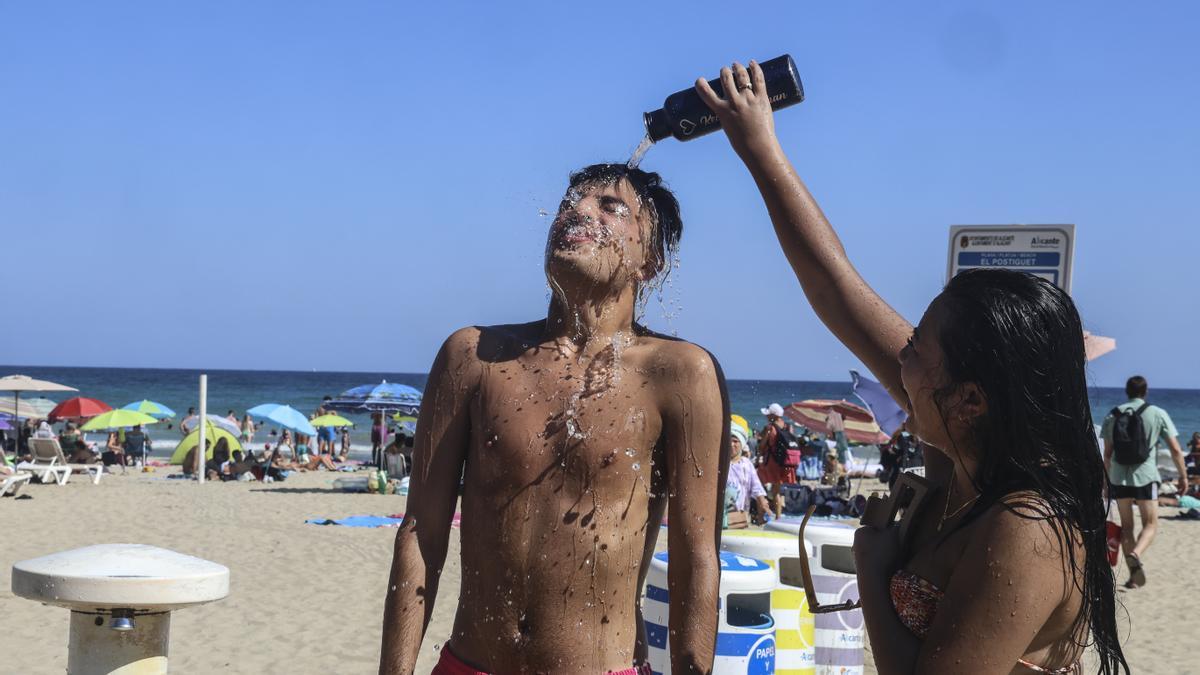Un joven refrescándose con agua en la playa del Postiguet de Alicante..