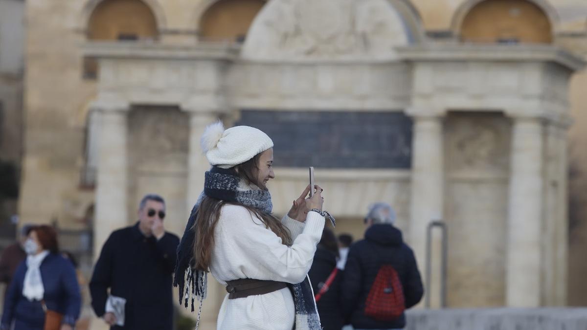 Una joven toma una foto en el Puente Romano de Córdoba, abrigada para el frío.