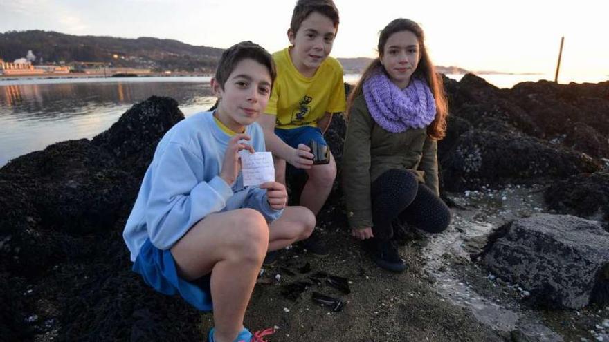 Borja, Martín y Luna, con la nota y los restos de la botella, en las rocas donde las encontraron. // G.Santos