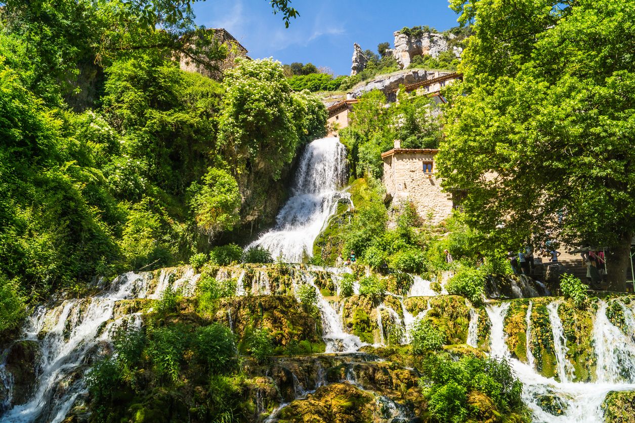 Cascada de agua entre árboles en día soleado, Orbaneja del Castillo.