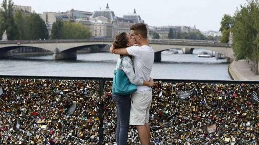 Una pareja se besa en uno de los puentes de París, lleno de candados del amor.