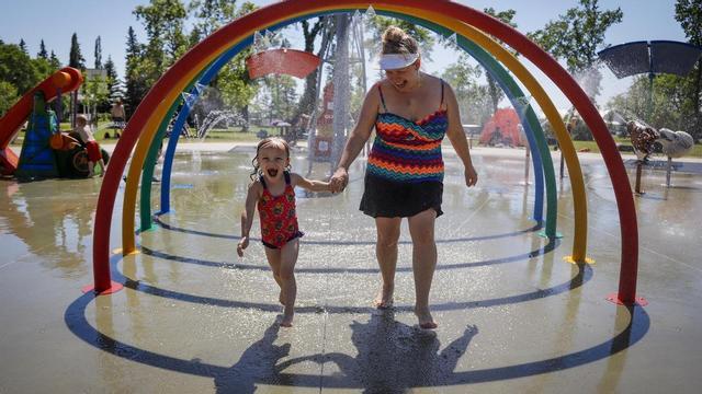 Una madre y su hija corren entre aspersores para tratar de vencer el calor en un parque.