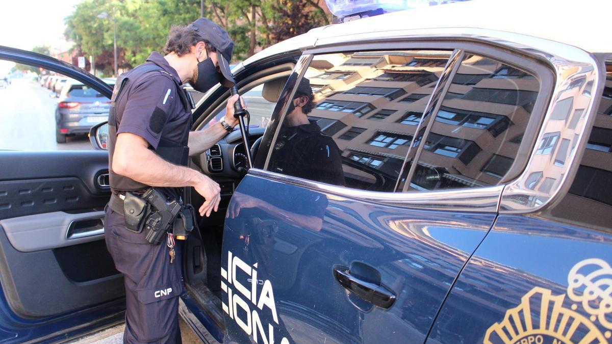 Un agente de Policía Nacional junto a un coche patrulla.