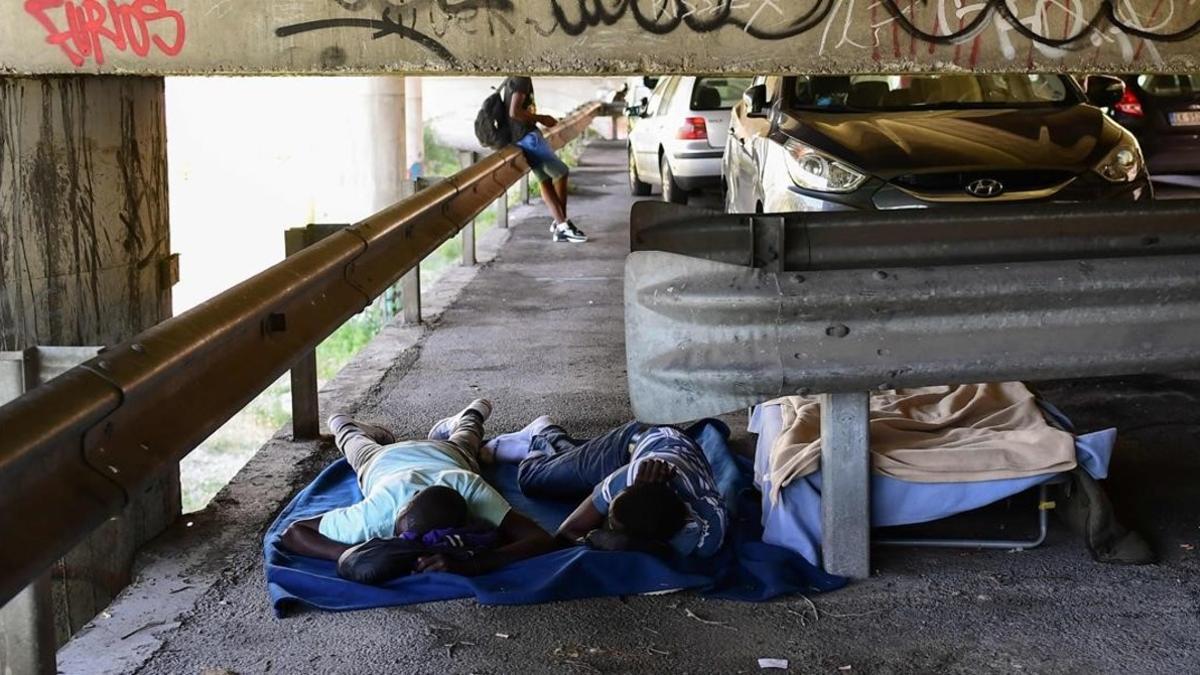 Unos inmigrantes tratan de descansar en el párking ubicado bajo un puente en la localidad italiana de Ventimiglia.