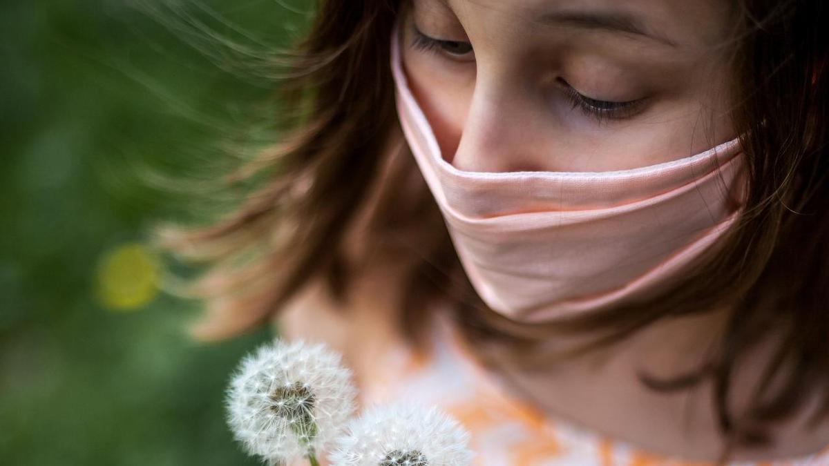 Una niña con mascarilla observa unas flores