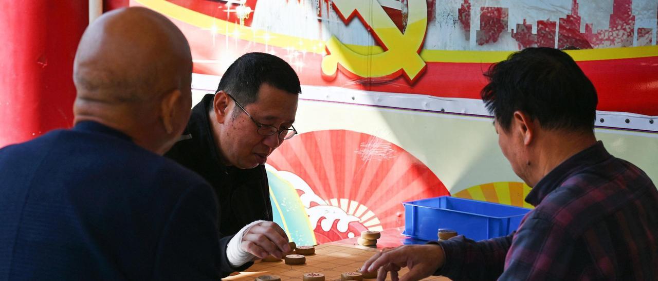 Dos hombres juegan al ajedrez chino, el 14 de enero, frente al emblema del Partido Comunista en un cartel de propaganda del congreso del partido del año 2017, en la isla de Pingtan, el punto más cercano de China a la principal isla de Taiwán