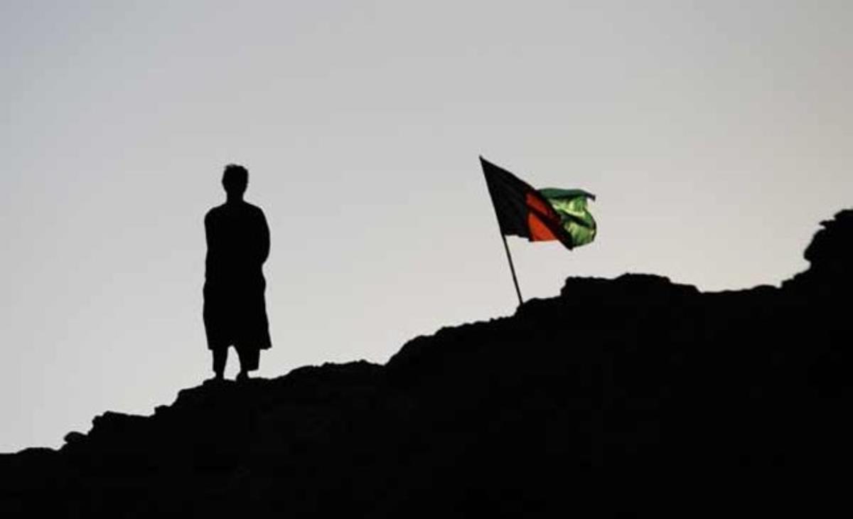 Un policia afganès observa, al costat de la bandera nacional, una patrulla que torna a la seva base al poble de Kunjak, al sud de la província de Helmand.