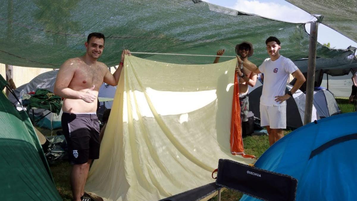 Tres jóvenes montan una tienda en la zona de acampada.