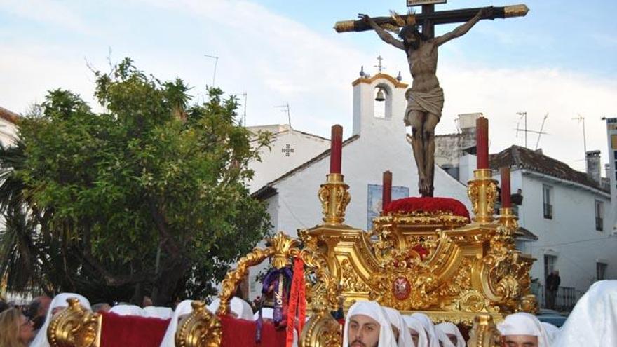 Hombres de trono portan al Cristo del Amor, con la ermita de Santiago al fondo, en la plaza Los Naranjos.