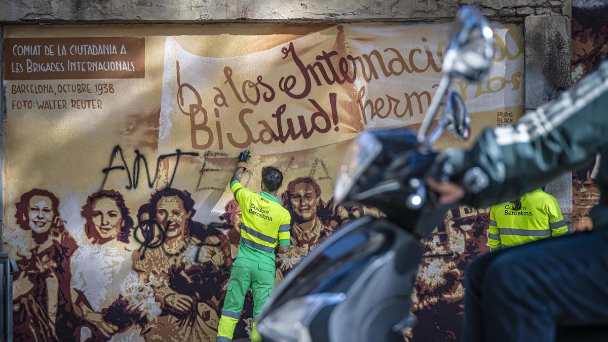 Un trabajador de la limpieza borra las pintadas del mural de recuerdo a las Brigadas Internacionales, en Barcelona.