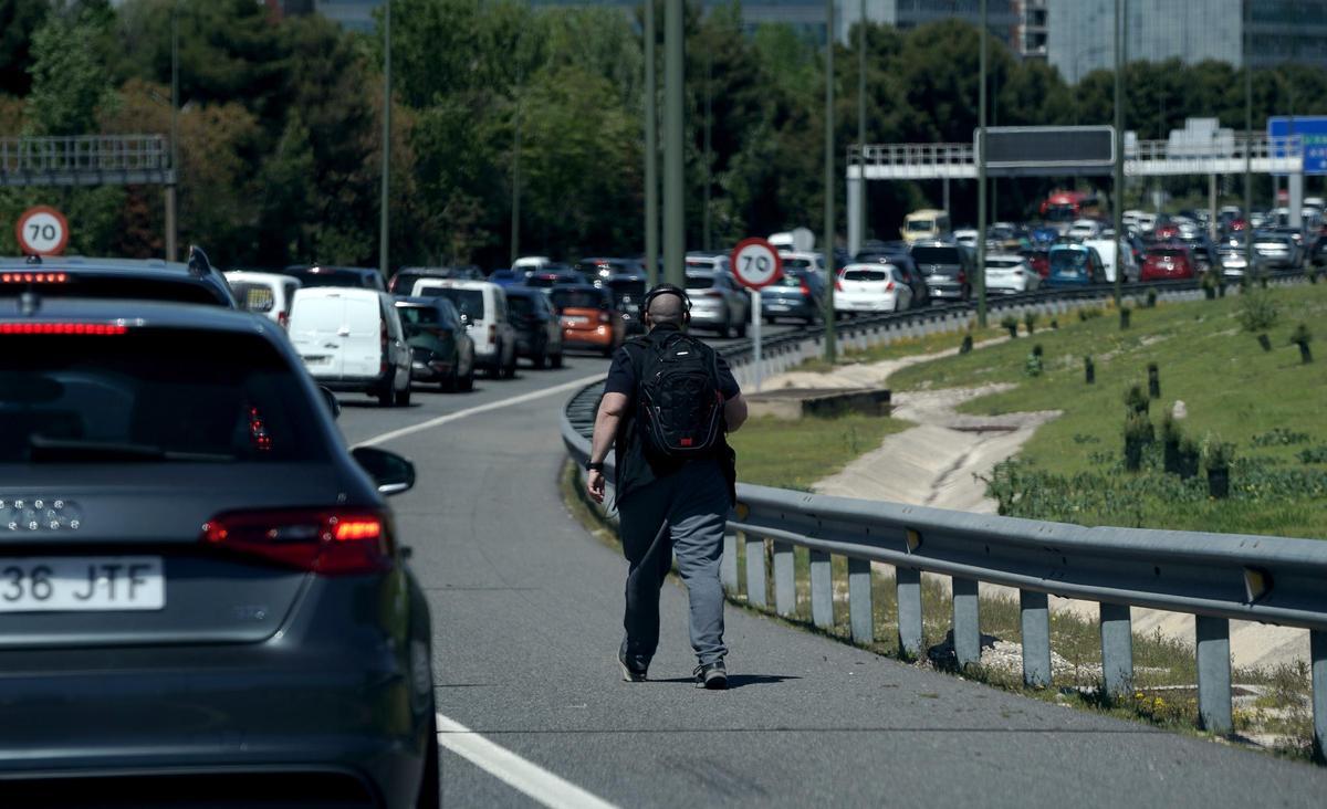 Un hombre, quizás harto de las retenciones, anda por una de las vías de acceso y salida de Madrid, este lunes