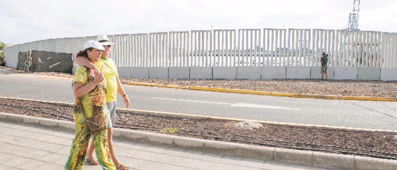 Una pareja camina por el paseo marítimo de Puerto del Rosario junto al cerramiento del muelle deportivo.